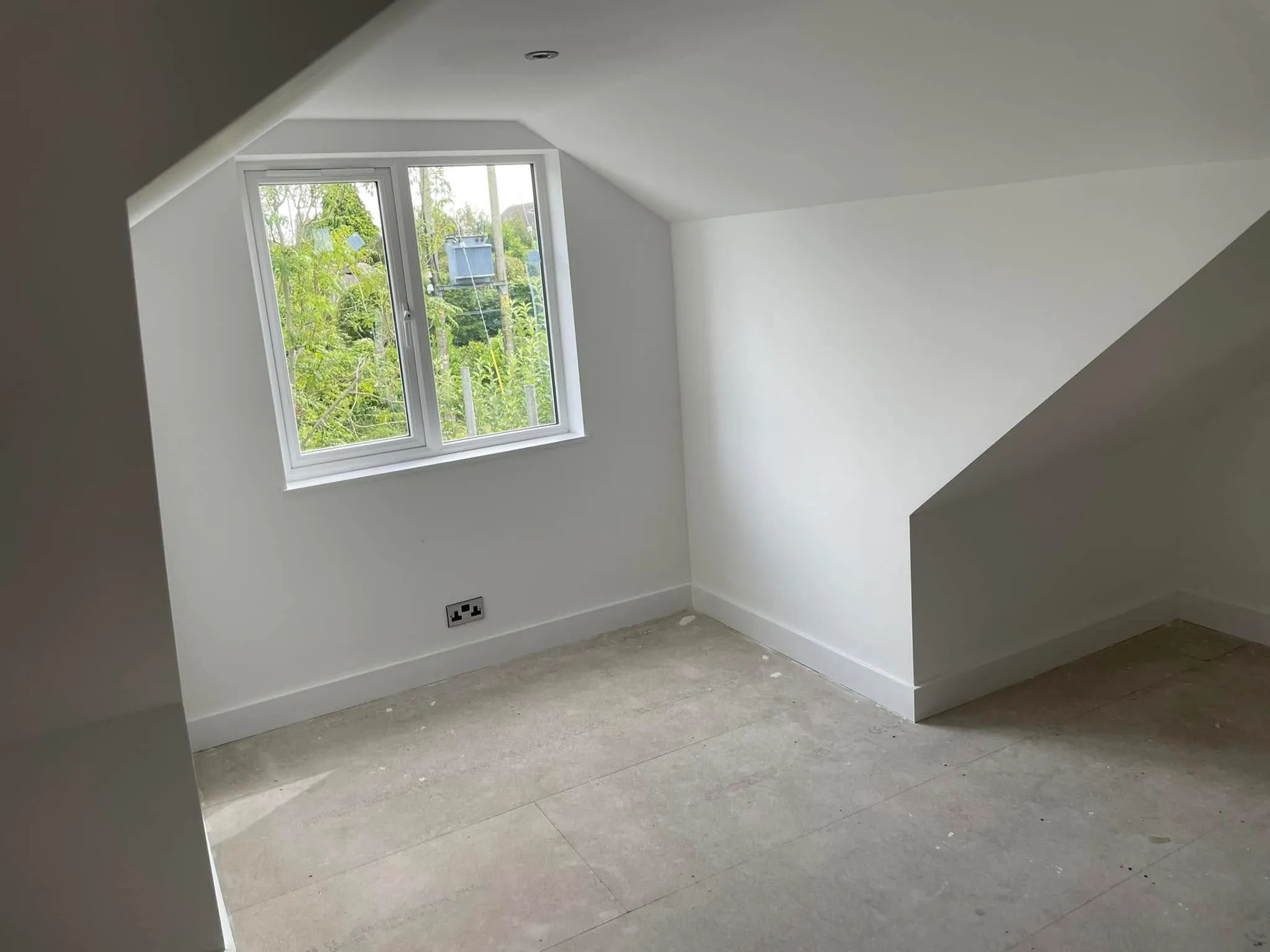 An empty room with a slanted ceiling and a window.