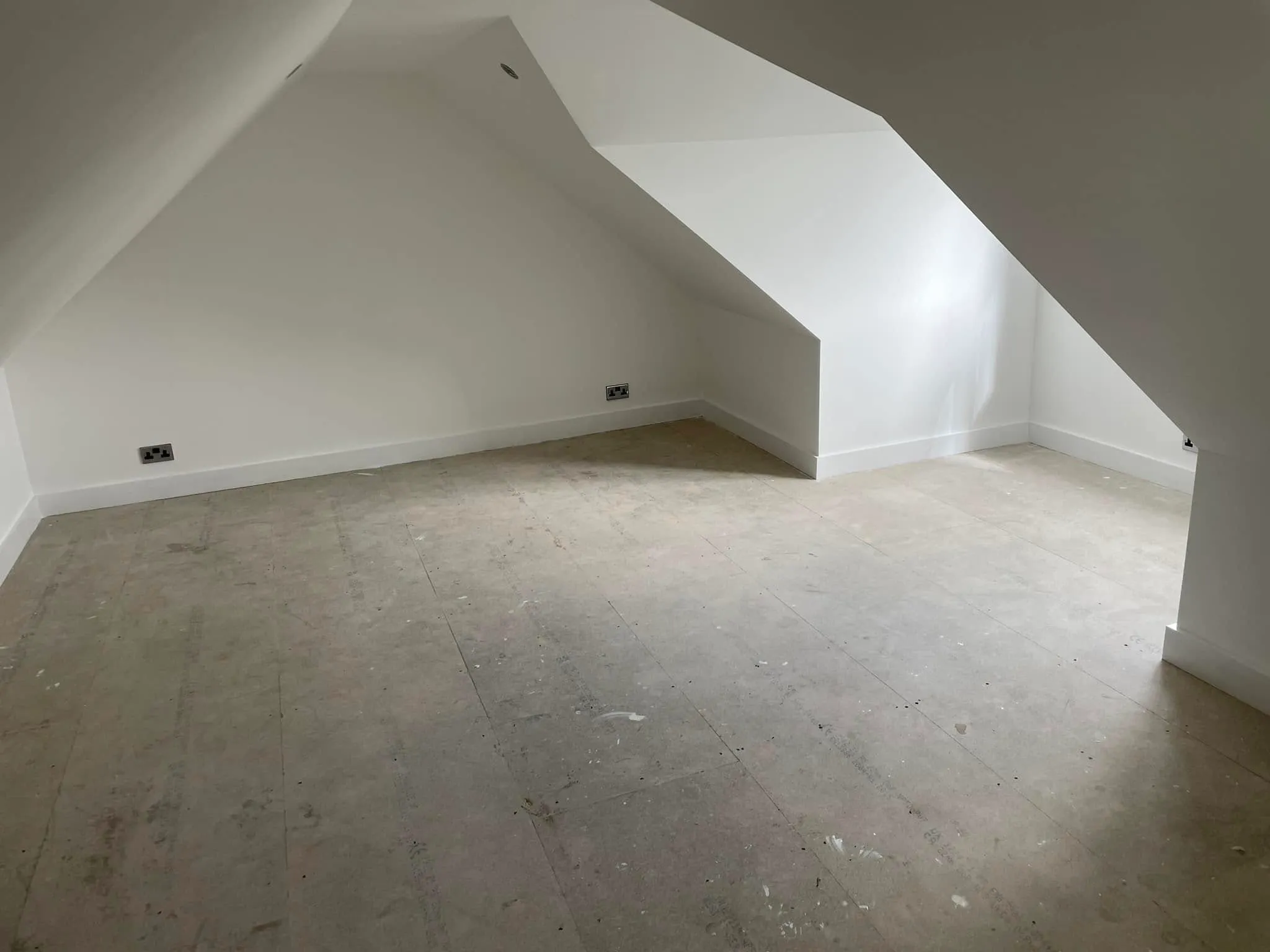 An empty room with a slanted ceiling and white walls.